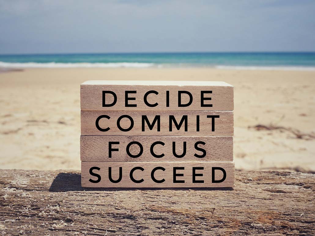 The words, "decide," "commit," "focus," and "succeed," written on blocks with a beach background scene